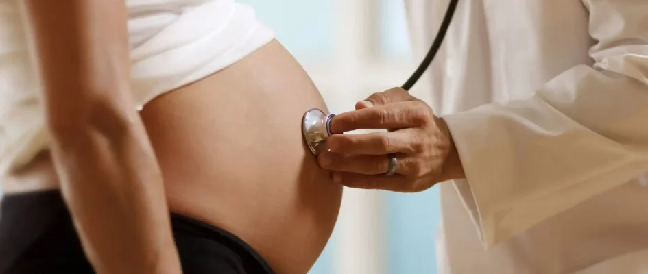 Doctor holding stethoscope to pregnant patient's belly