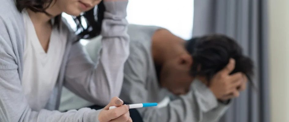 Woman sitting alongside partner holding pregnancy test in hand