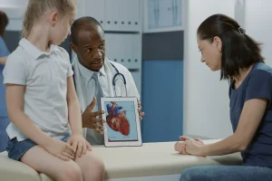 Child in Doctor's room with Dr showing a diagram of a heart to mother and patient